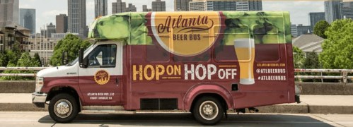 A colorful beer tour van with "Hop On Hop Off" text, parked on a city street with buildings in the background.