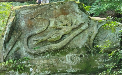 A carved stone depicting a mermaid entwined with a serpent, surrounded by lush greenery.