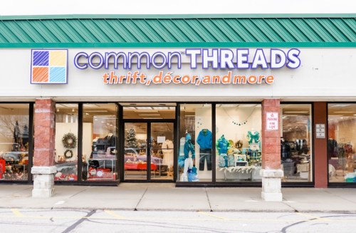 Exterior of a thrift store named "commonTHREADS," featuring a colorful sign and large windows displaying various items.
