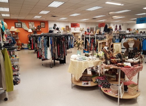 A spacious thrift store interior with racks of clothing and displays of vintage items and accessories.