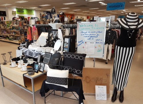 Display of clothing and home goods at a thrift store, featuring a sign welcoming customers and a mannequin in a striped outfit.