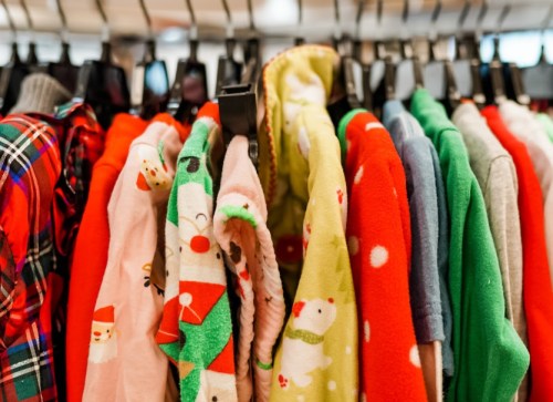 A colorful display of festive clothing, including red, green, and patterned sweaters, hanging on a rack.