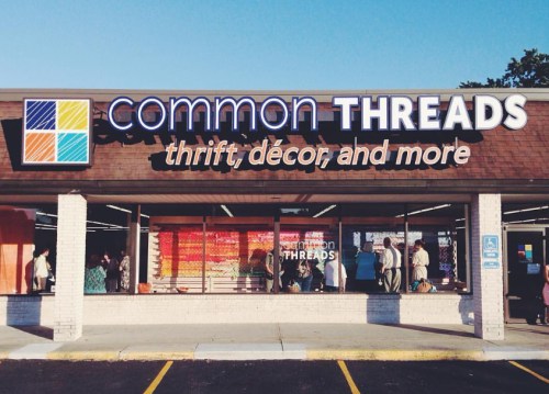 Exterior of a thrift store named "common THREADS," featuring colorful signage and people browsing inside.