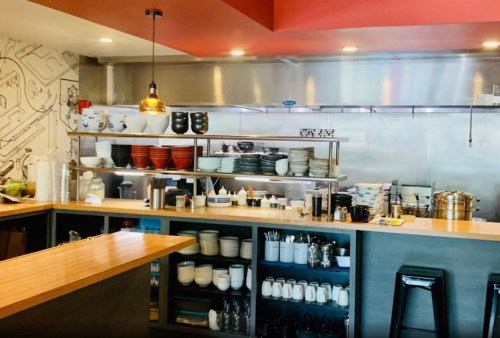 A modern kitchen counter with shelves of dishes, utensils, and cooking equipment, featuring a warm, inviting atmosphere.