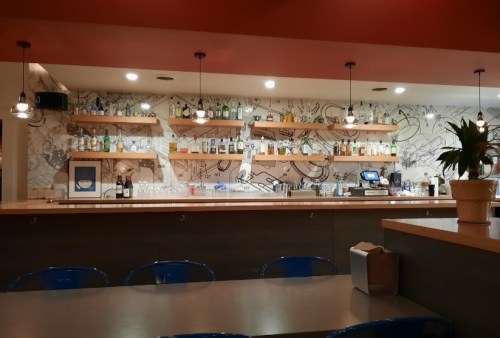 A modern bar with shelves of bottles, a stylish counter, and artistic wall decor in a cozy setting.