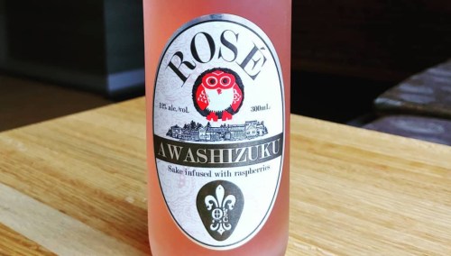 A bottle of rosé sake infused with raspberries, featuring a decorative label with an owl and floral design.