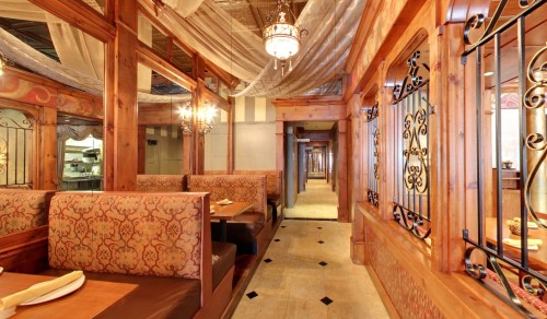 Cozy restaurant interior featuring wooden decor, plush seating, and elegant chandeliers along a spacious corridor.