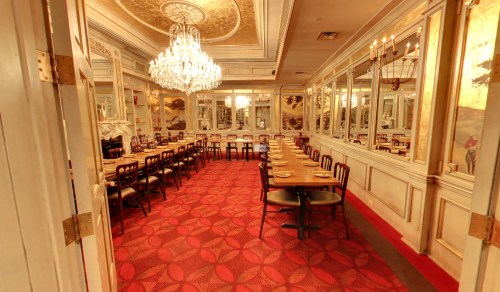 Elegant dining room with a chandelier, mirrored walls, and long tables set on a red carpet.
