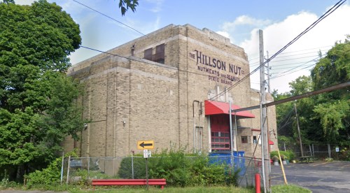 A large brick building with a red roof, featuring the sign "The Hillson Nut Co." and surrounded by trees and a fence.