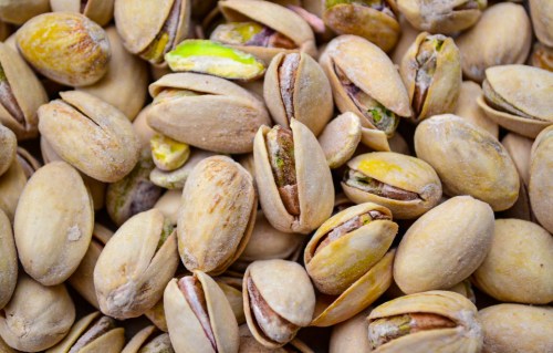 A close-up of various pistachio nuts in their shells, showcasing their beige and green hues.
