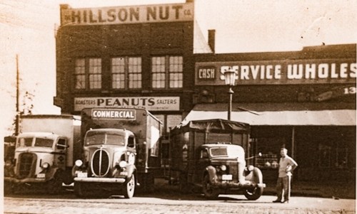 Historic photo of Hillson Nut Co. with vintage trucks parked outside and a man standing nearby.