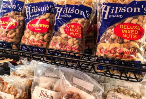 A display of Hillson's brand nut packages, including salted cashews and deluxe mixed nuts, on a store shelf.