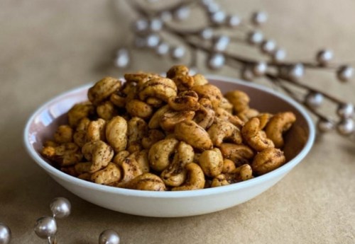 A bowl of spiced cashews on a textured surface, surrounded by decorative pearls.