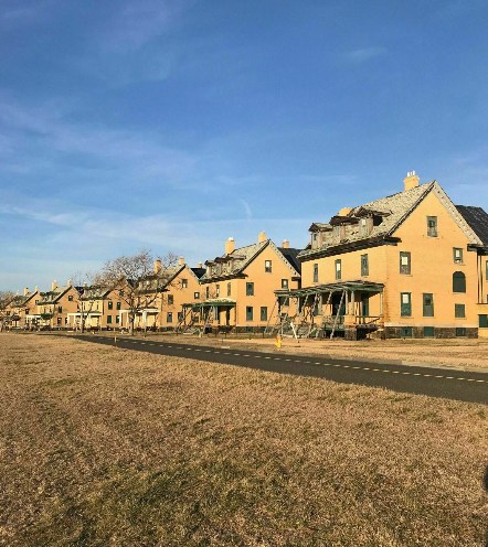 A row of yellow houses with porches under a clear blue sky, set against a grassy landscape.