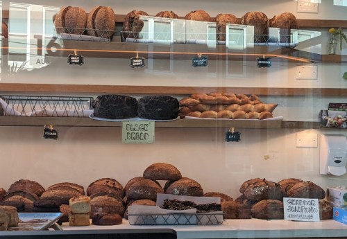 A display of various breads and pastries, including loaves, rolls, and a sign for cheddar jalapeño bread.