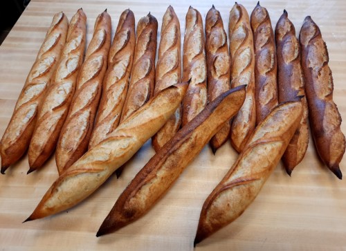 A variety of freshly baked baguettes arranged neatly on a wooden surface.