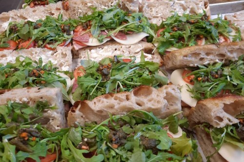 A close-up of sandwiches filled with layers of salami, mozzarella, tomatoes, and topped with fresh arugula.