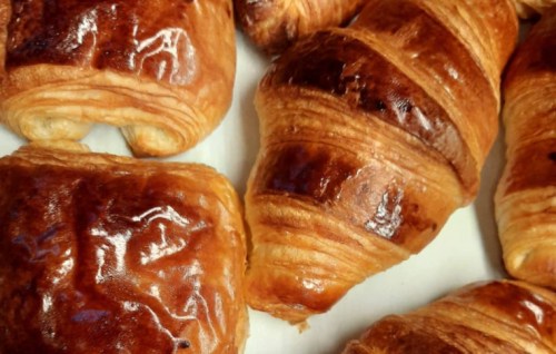 A close-up of freshly baked golden-brown croissants and pastries on a white surface.