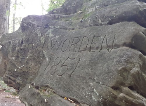 Carved rock with the inscription "J. H. M. Worden 1851" surrounded by trees in a natural setting.