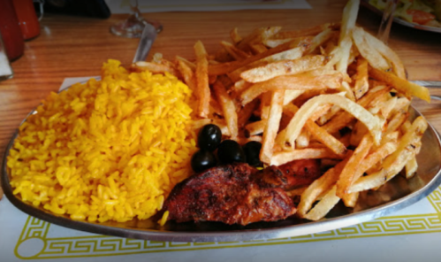 A silver platter with yellow rice, crispy fries, and a piece of grilled meat garnished with black olives.