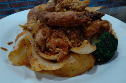 A plate of flavorful chicken with onions, potatoes, and broccoli, garnished with spices and sauce.