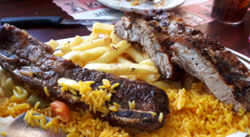 A plate of yellow rice topped with grilled meat and served with French fries.