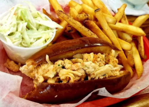 A plate featuring a lobster roll, coleslaw, and crispy French fries on a red tray.