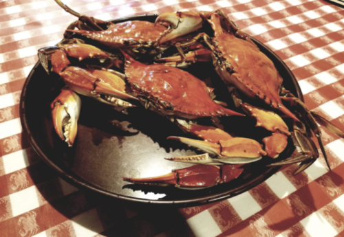 A black plate filled with cooked crabs, resting on a red and white checkered tablecloth.