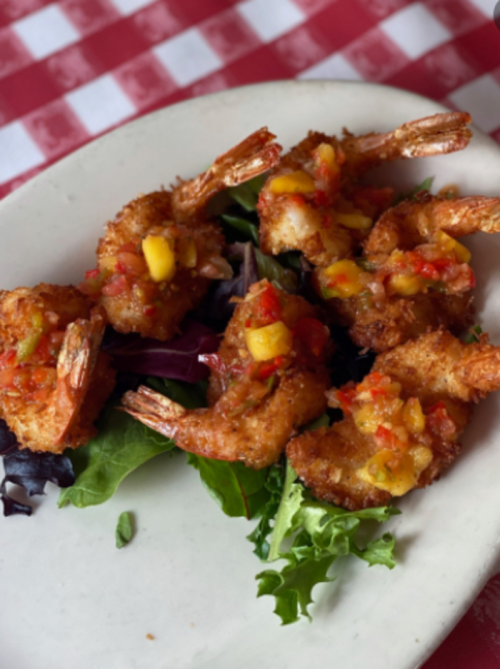 Crispy fried shrimp topped with mango salsa, served on a bed of mixed greens on a white plate.