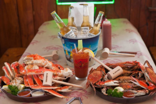 A table set with two trays of crabs, a cocktail, and a bucket of Corona beers, all in a rustic dining setting.