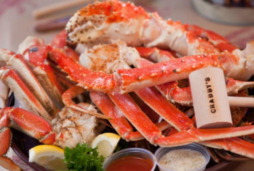A platter of cooked crab legs with lemon wedges and dipping sauces, featuring a wooden marker labeled "Crabby's."