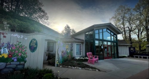A charming building with large windows, colorful murals, and pink chairs, set against a sunset backdrop.