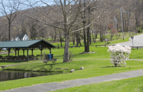 A peaceful park scene with a pavilion, blooming flowers, and a pond, surrounded by green grass and trees.