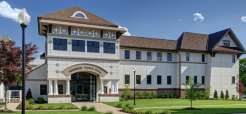 Modern town hall building with a large entrance, landscaped grounds, and a clear blue sky in the background.