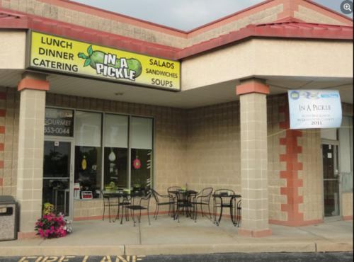 Exterior of "In a Pickle" restaurant featuring a sign, outdoor seating, and a banner for an award.
