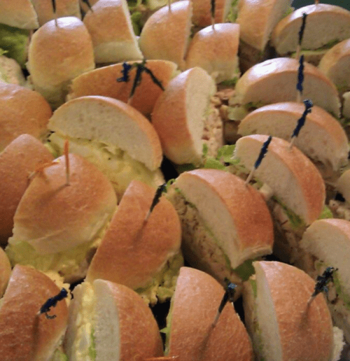 A close-up of several sandwiches with lettuce, filled with egg and chicken salad, each secured with a toothpick.