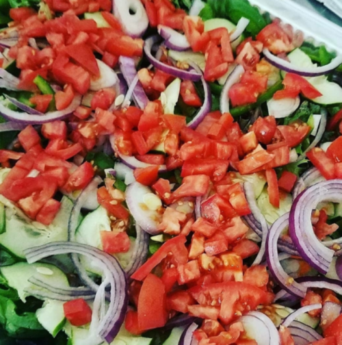 A colorful salad with chopped tomatoes, red onions, cucumbers, and leafy greens arranged in a tray.