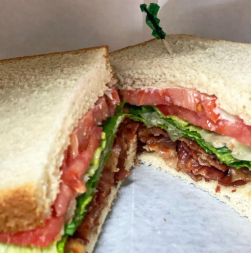 Close-up of a sandwich with layers of lettuce, tomato, and bacon, held together with a toothpick.