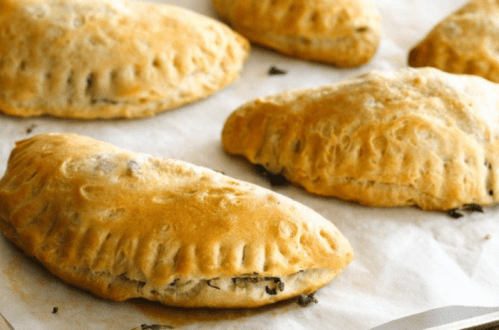 Golden-brown baked pastries filled with greens, arranged on parchment paper.