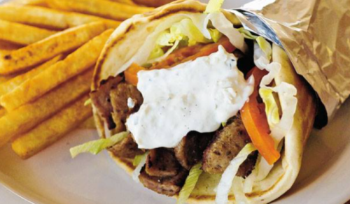 A wrapped sandwich filled with meat, lettuce, tomato, and sauce, served with a side of golden fries.