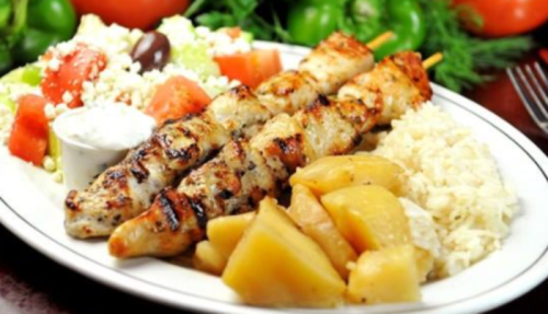 Grilled chicken skewers served with rice, sautéed apples, salad, and a side of yogurt sauce.