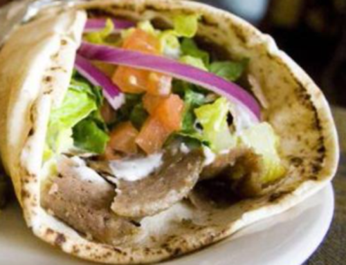 A close-up of a wrapped pita filled with sliced meat, lettuce, tomatoes, onions, and sauce.