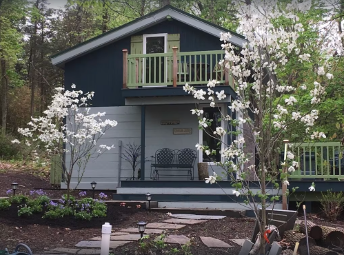 A charming blue house with a green balcony, surrounded by blooming white flowers and landscaped gardens.