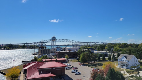 A scenic view of a bridge over water, with buildings and trees in the foreground under a clear blue sky.