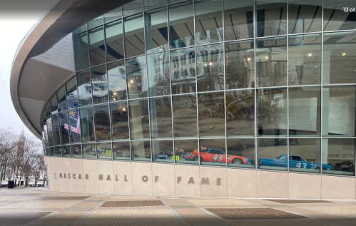 Exterior view of the NASCAR Hall of Fame, featuring large glass windows and colorful race cars on display inside.