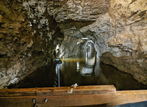 A dimly lit underground tunnel with water reflecting the rocky walls, creating a mysterious atmosphere.