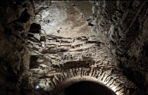 A rocky cave ceiling with textured stone formations and subtle lighting illuminating the surface.