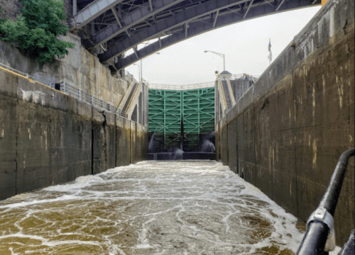 View from inside a lock, showing rushing water and a green gate under a bridge.