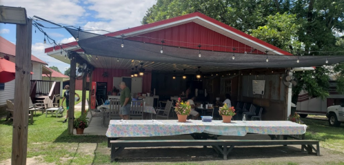 A rustic outdoor dining area with string lights, tables adorned with flowers, and people enjoying the space.