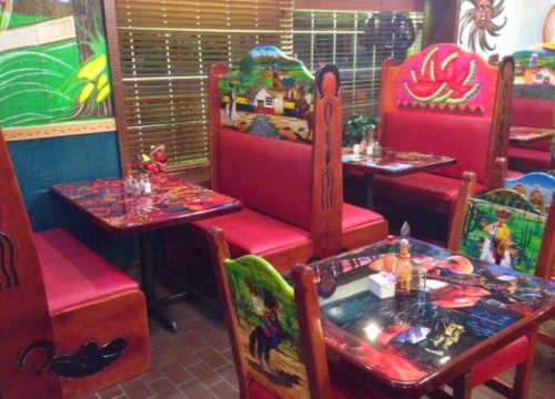 Colorful restaurant interior featuring vibrant murals on booths and tables, with red seating and wooden decor.